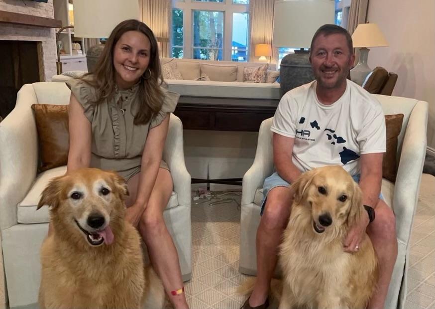 Woman with a golden retriever in front of her and man with a golden retriever in front of him