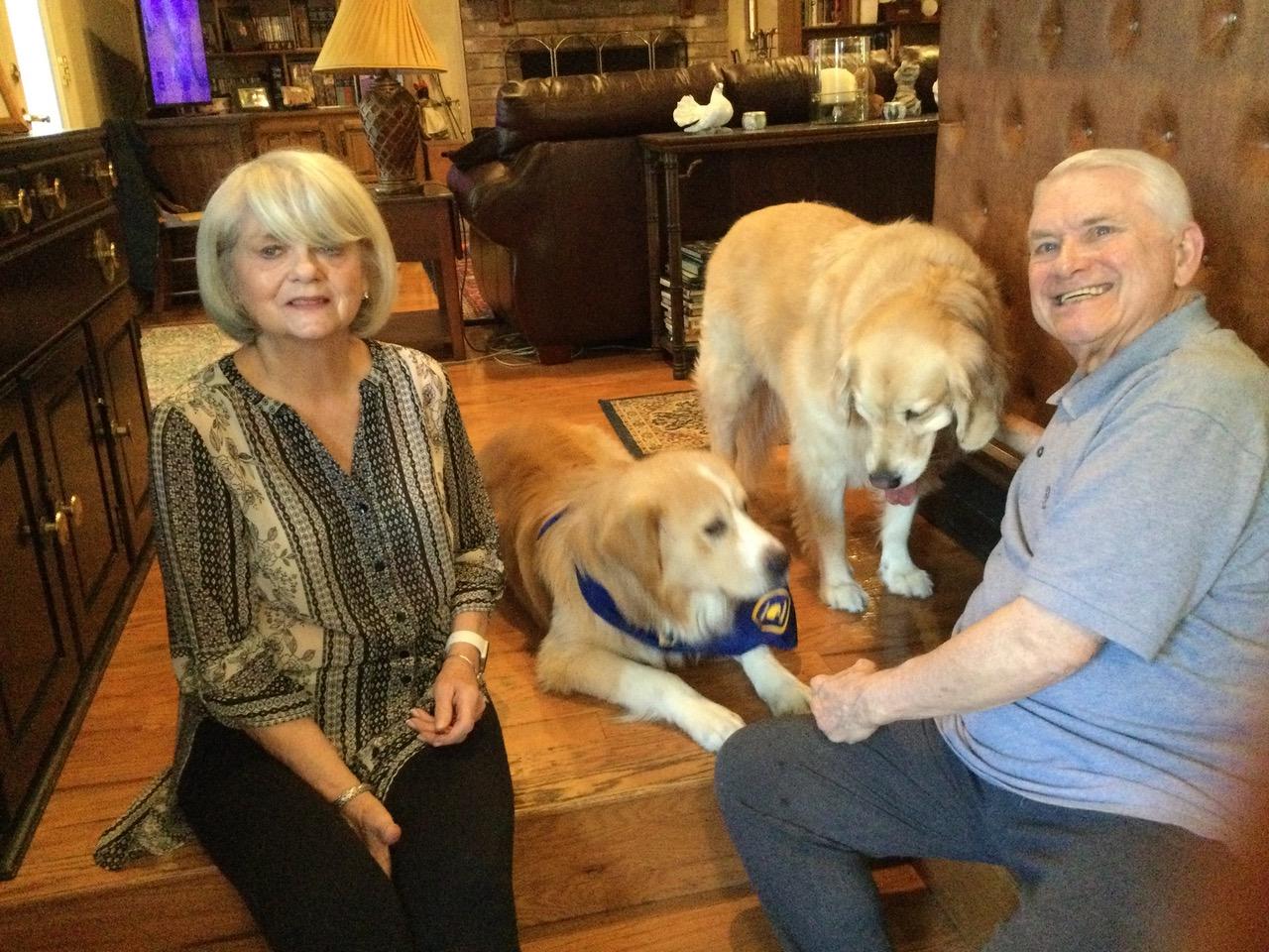 Older couple sitting on floor with two golden retrievers