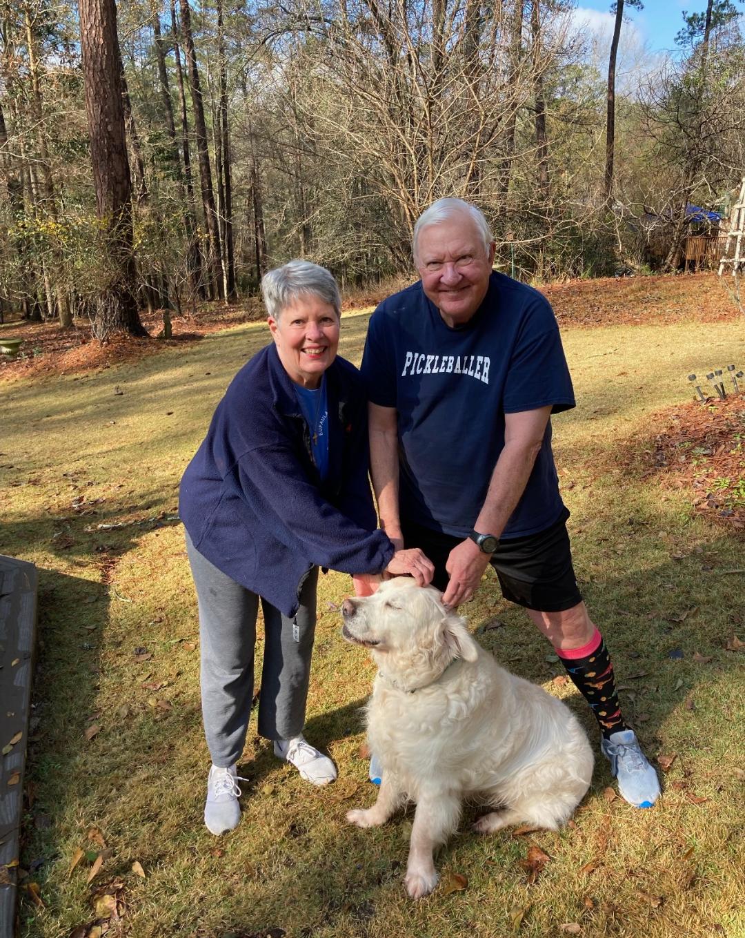 Older couple petting a white golden retriever sitting in front of them