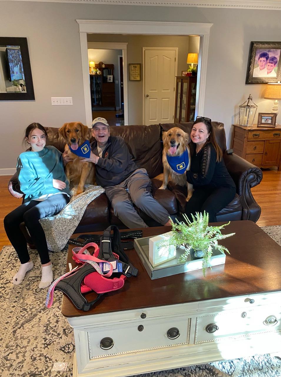 Family of three sitting on couch with two golden retrievers