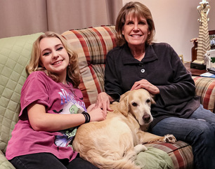 Girl and woman sitting on couch with a golden retriever between them