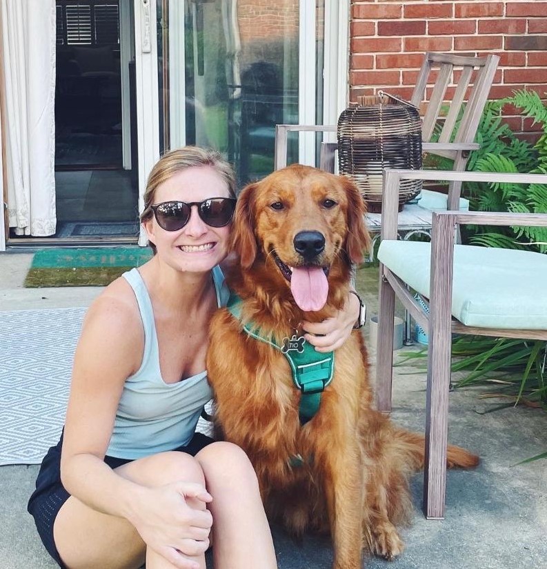 Woman sitting down with her arm around a golden retriever sitting next to her
