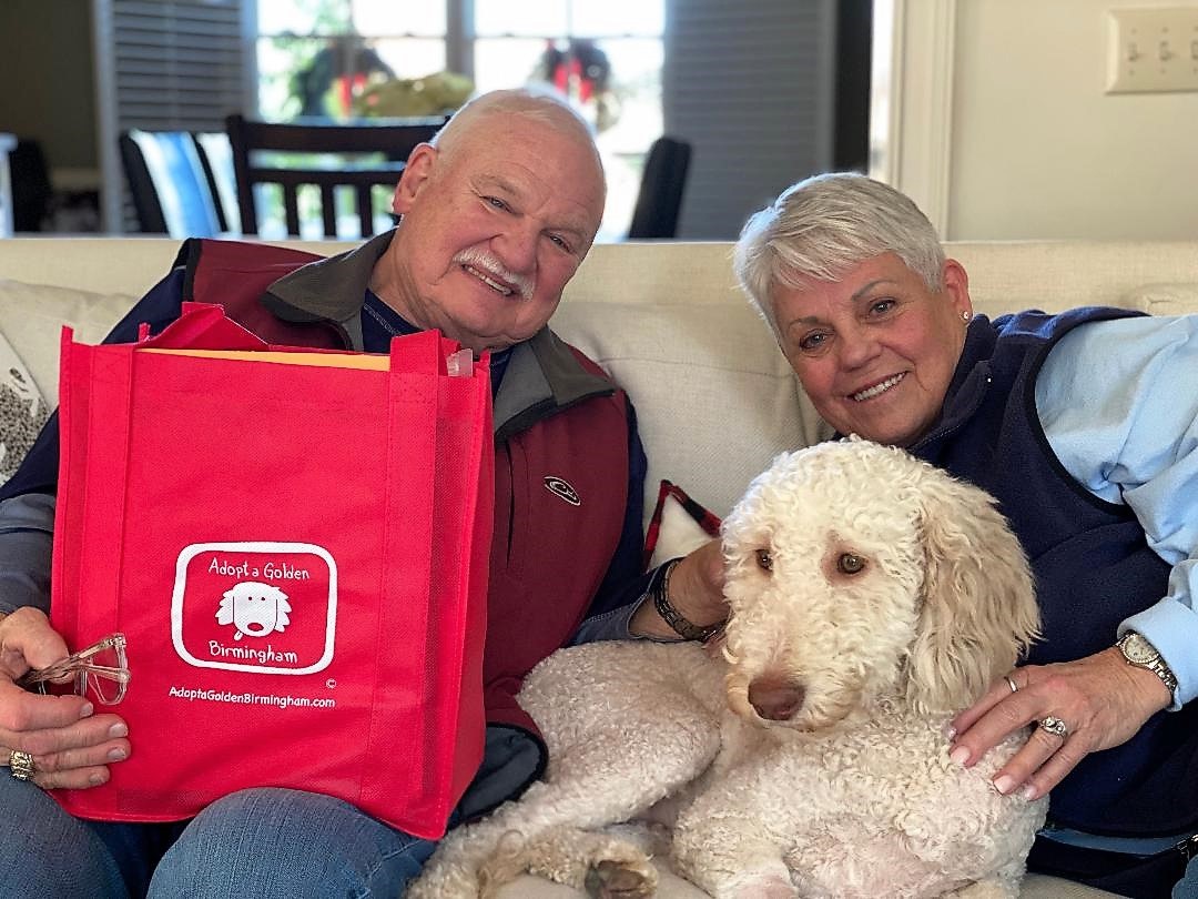Older couple sitting on a white couch with a golden doodle between them