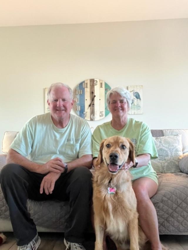 Older couple sitting on the couch with a golden retriever in front of them
