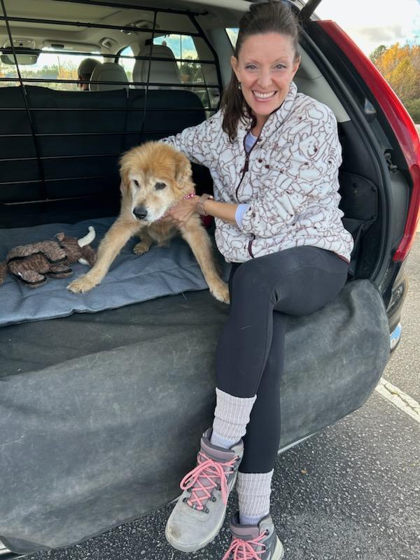 Woman sitting in the trunk of car holding a golden retriever mix puppy