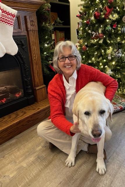 Old woman sitting on the floor with a golden retriever in front of a Christmas tree