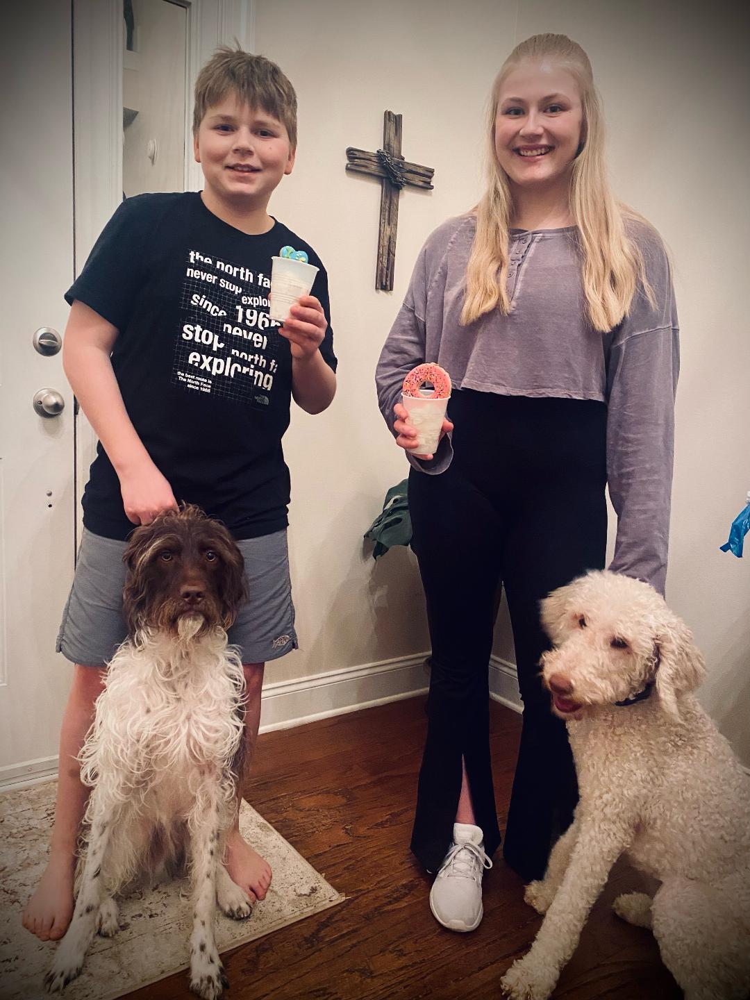 Brother and sister holding dog treats with two dogs next to them