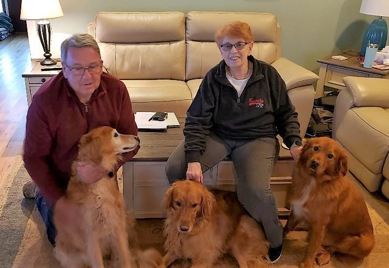Older couple sitting down with three golden retrievers