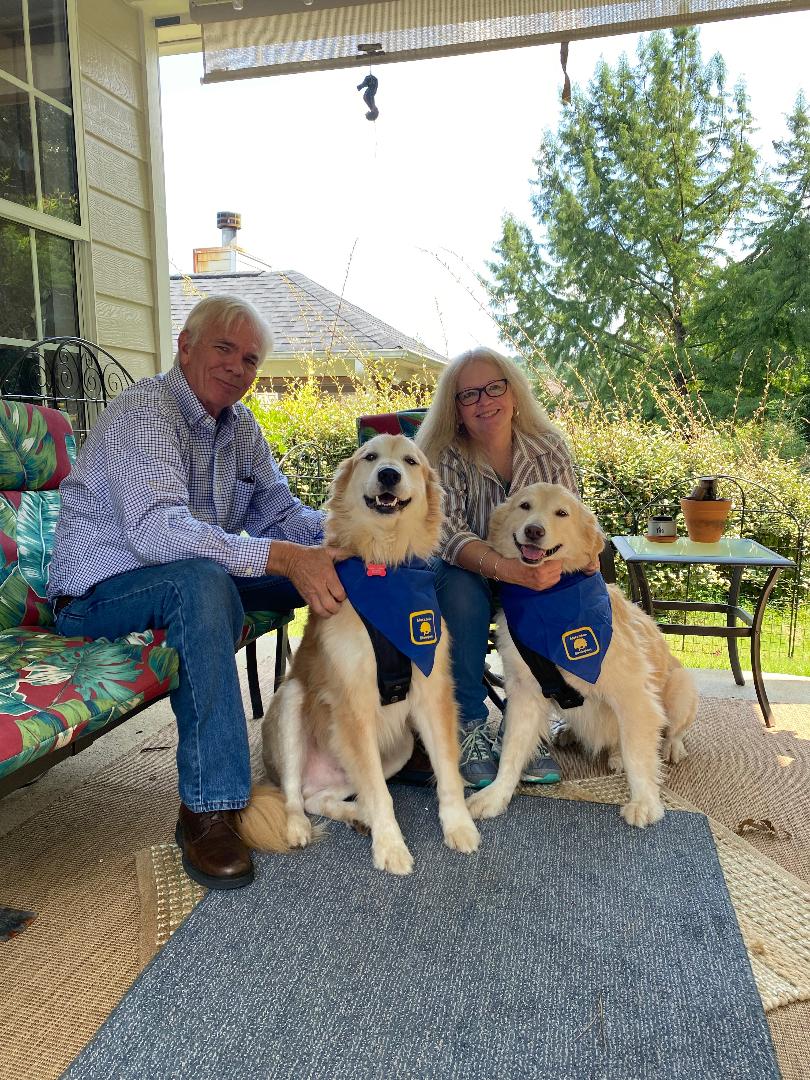 Older couple sitting on patio with two golden retrievers