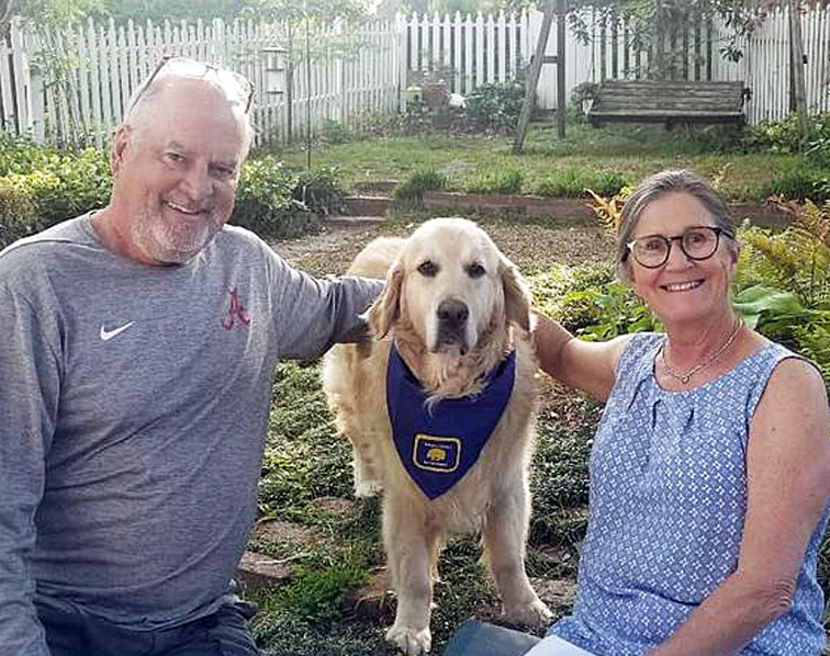 Older couple sitting with arms around a golden retriever in between them