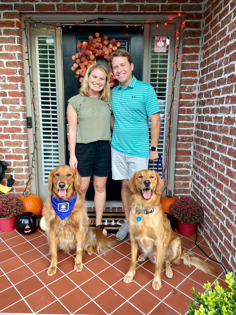 Woman and man standing in front of front door with two golden retrievers