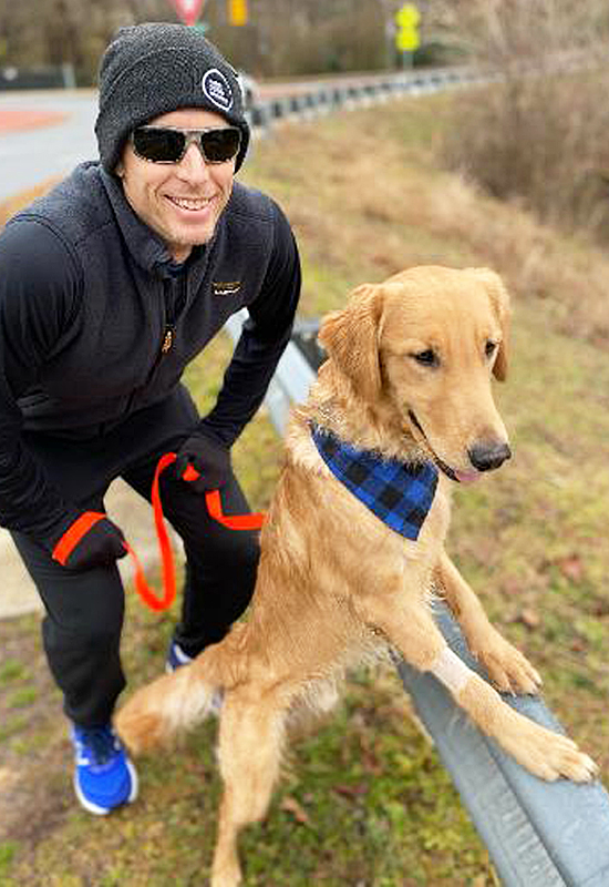 Man squatting next to golden retriever with front legs up on guard rail